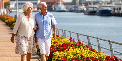 Ventspils promenāde ar ziediem un senioru pāri pie ostas